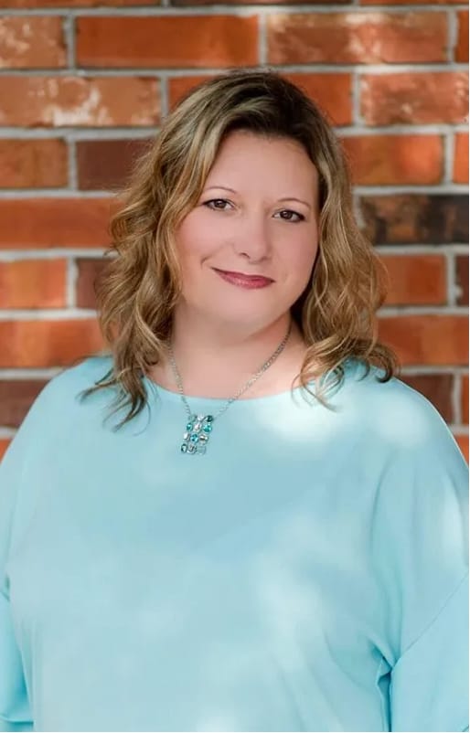 Picture of Dr. Christina smiling in a blue shirt. She is standing against a brick wall
