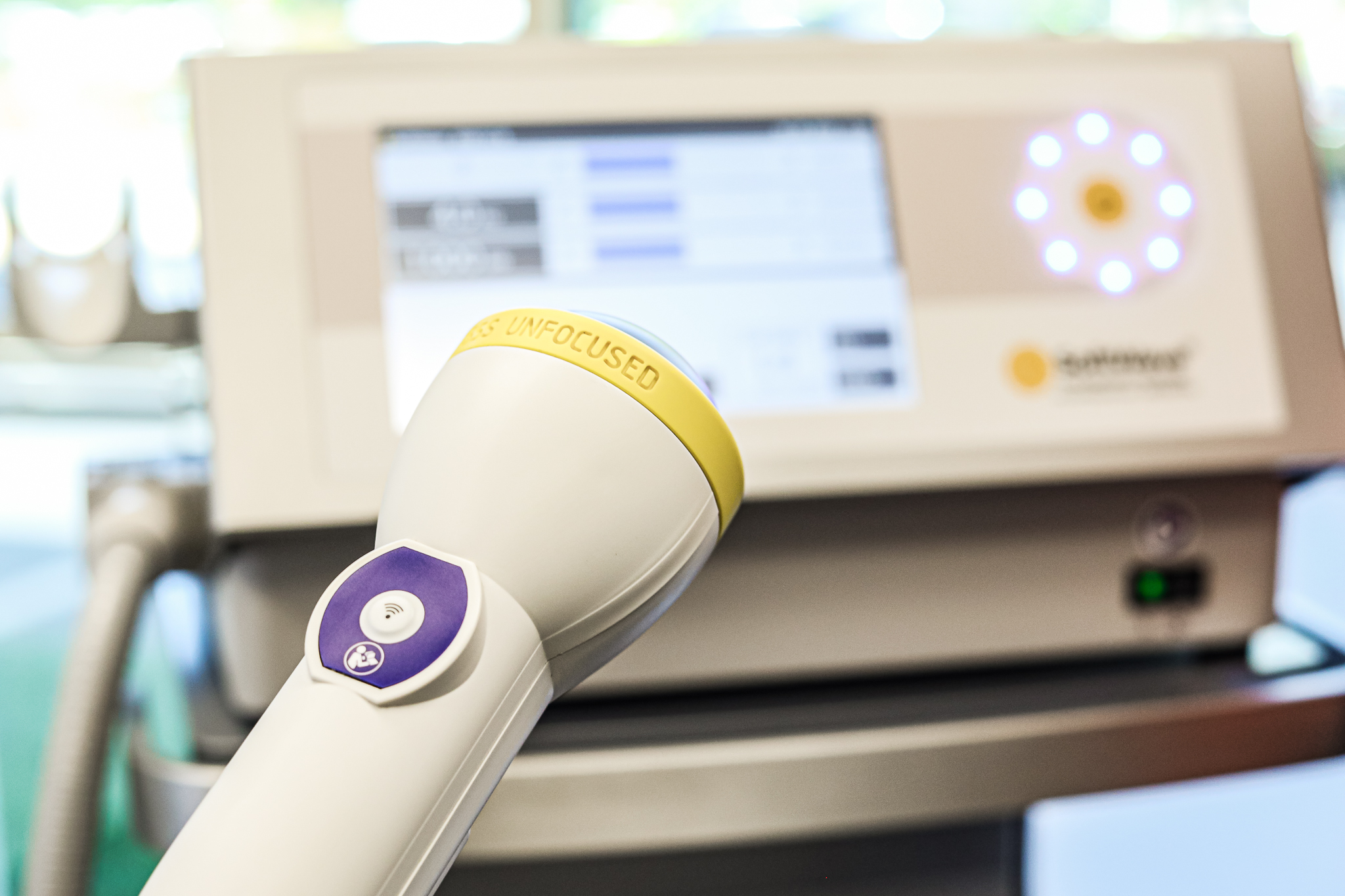 A chiropractor applying a Softwave therapy applicator to a patient's shoulder. The patient is sitting comfortably and looks relaxed. The clinic is modern, bright, and clean.